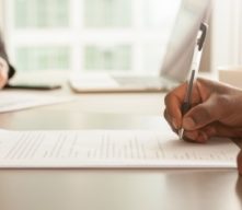 Person signing paperwork with mortgage officer in the background.