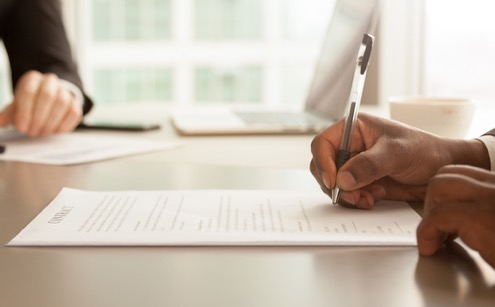 Person signing paperwork with mortgage officer in the background.