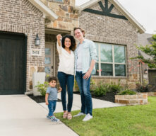Young couple with one child in front of new home holding keys