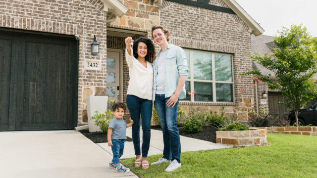 Young couple with one child in front of new home holding keys