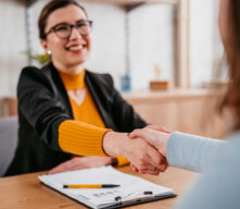 Woman shaking hands with person and paperwork is sitting on top of a table.