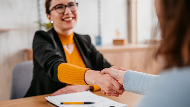 Woman shaking hands with person and paperwork is sitting on top of a table.