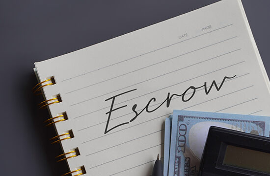 Close up image of calculator and money with escrow written on a lined notepad.