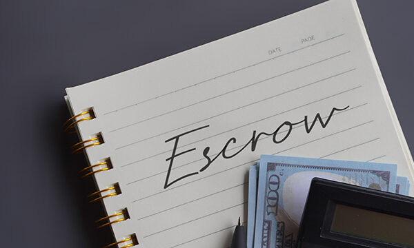 Close up image of calculator and money with escrow written on a lined notepad.