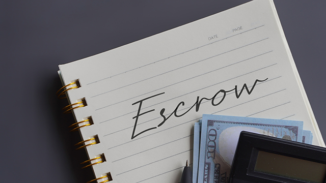 Close up image of calculator and money with escrow written on a lined notepad.