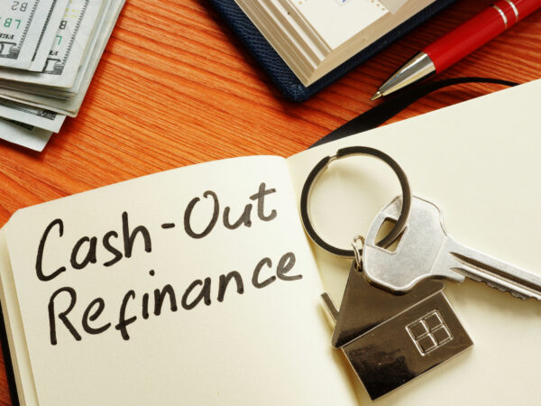 Notebook sitting on a wood table opened to a page that says Cash-Out refinance with a house key sitting on top.