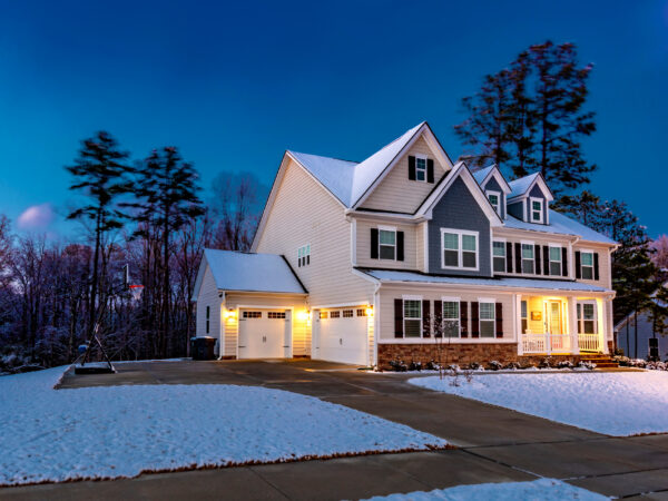 A two-story home at dusk with light snow covering the grass and the roof.