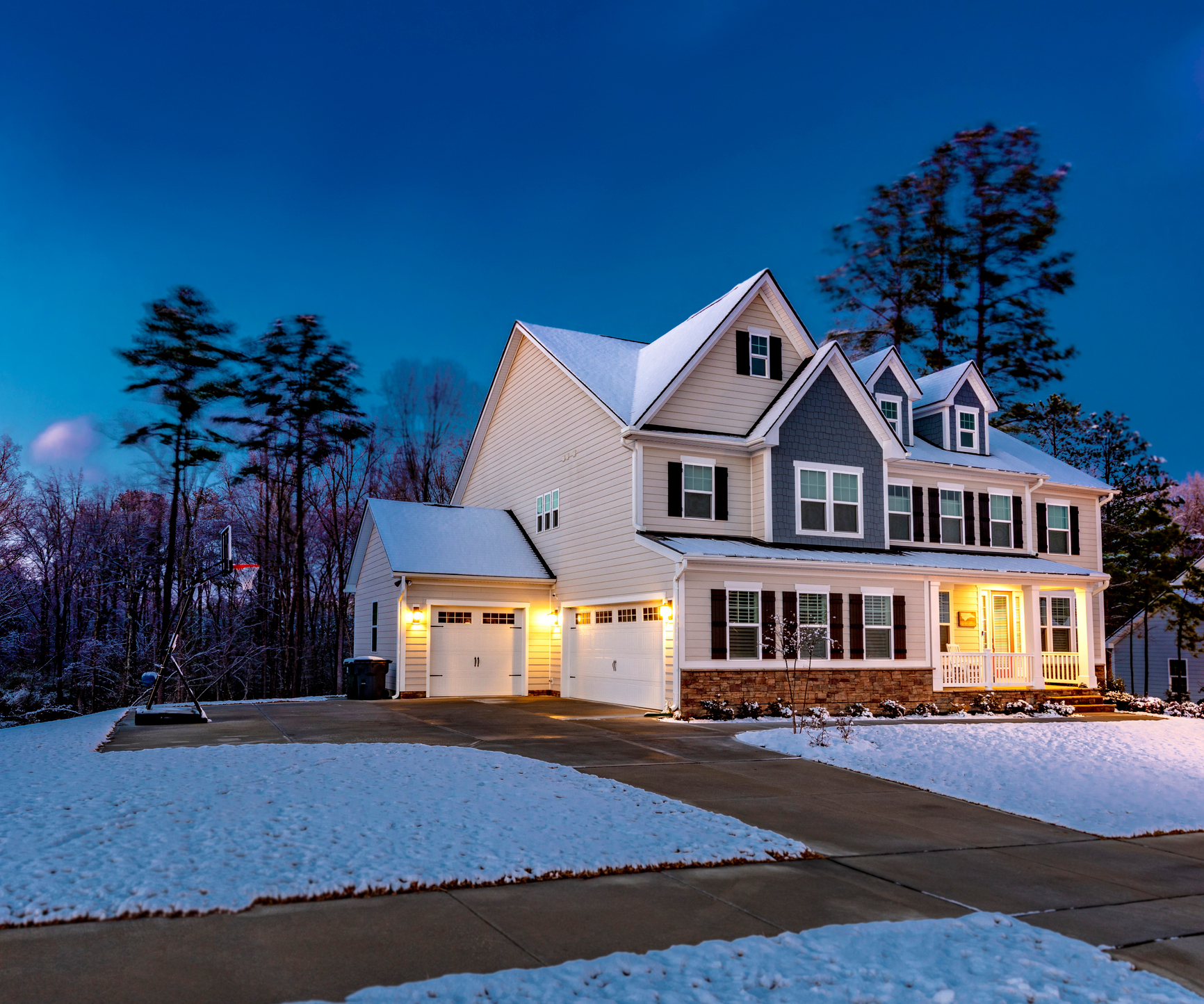 A two-story home at dusk with light snow covering the grass and the roof.