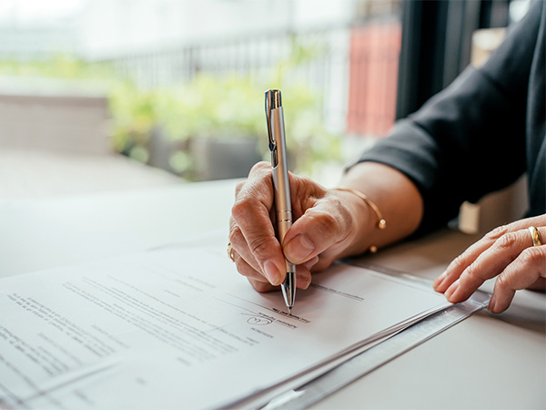 Close up of hand holding pen and signing mortgage documents.